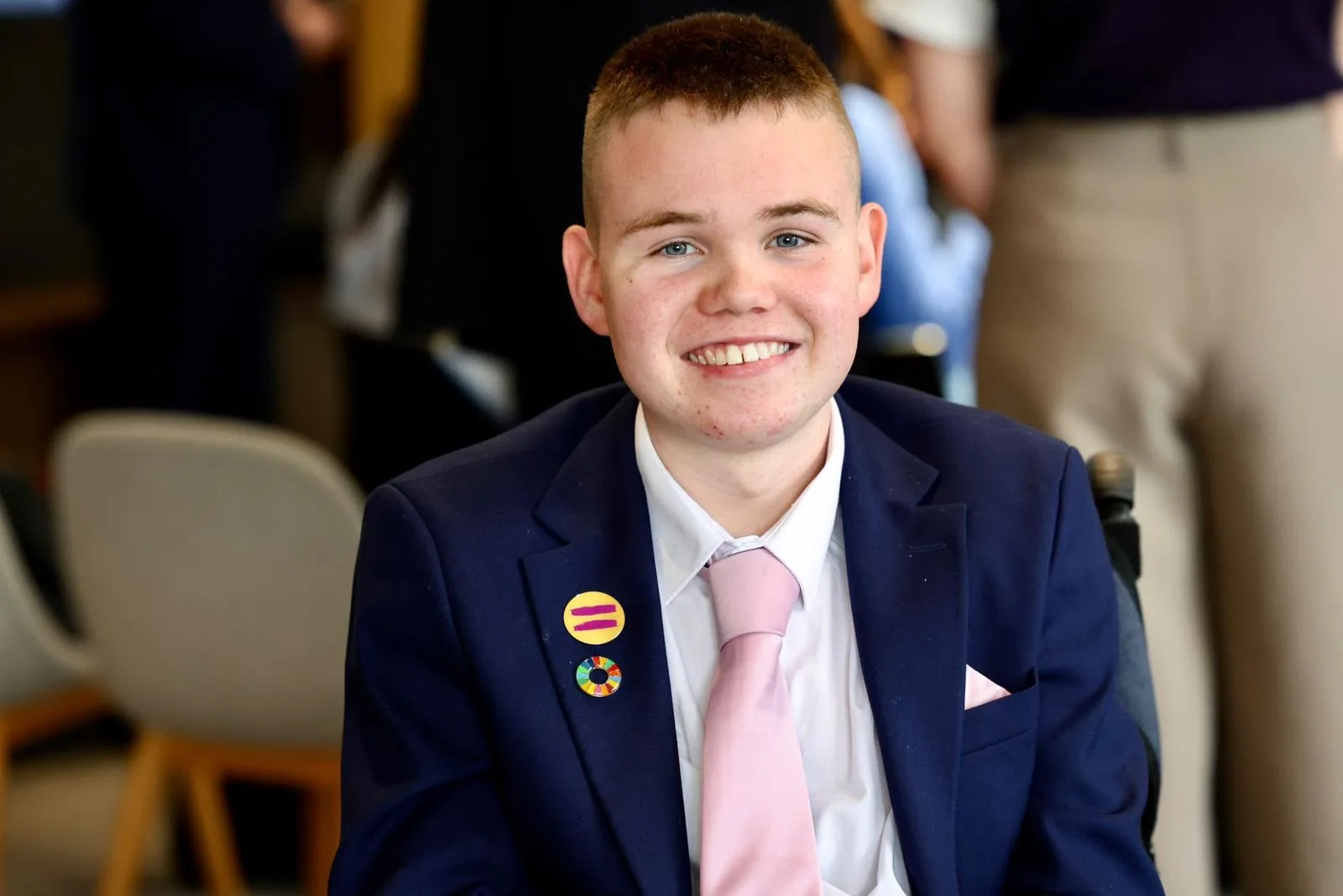 James Casserly smiling, wearing a navy suit and pink tie